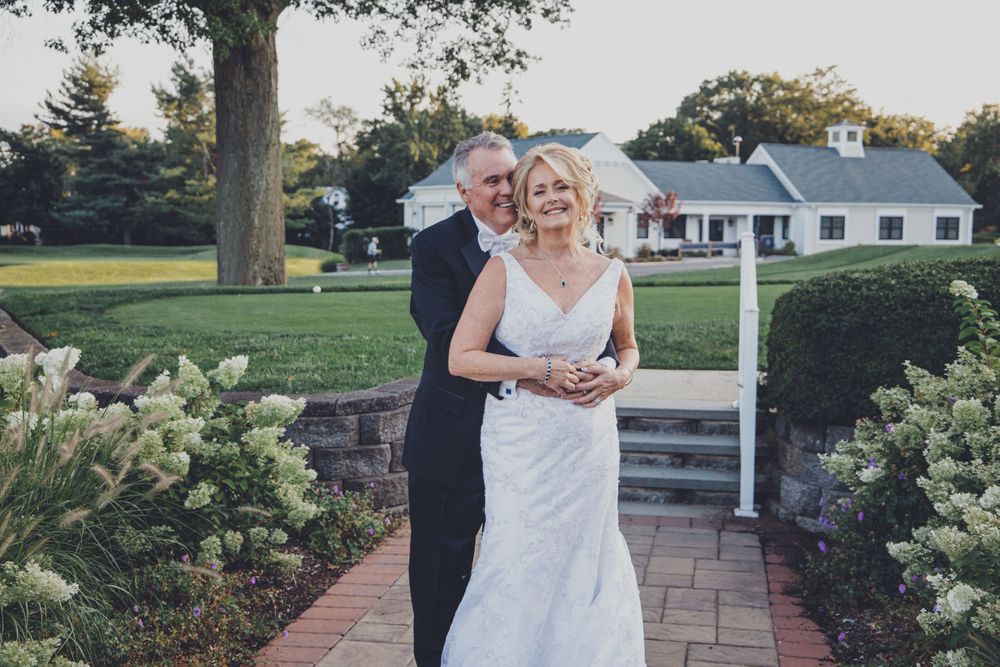 Couple takes wedding portraits along a stone pathway with white hydrangeas in bloom.