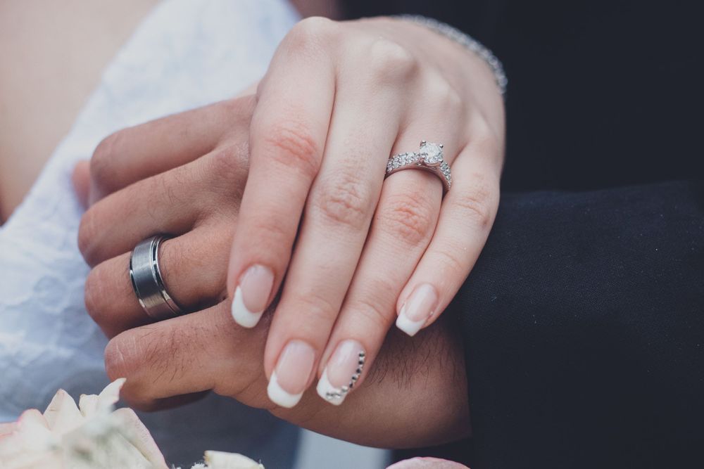 Wedding rings showcased on hands with delicate manicures against a dark backdrop.