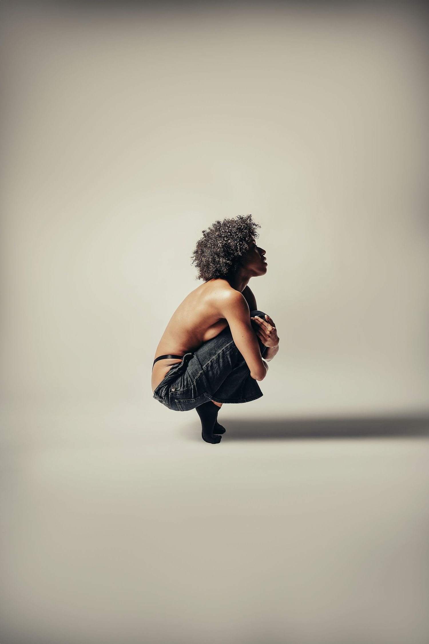 Minimalist studio portrait of figure crouching against light background.