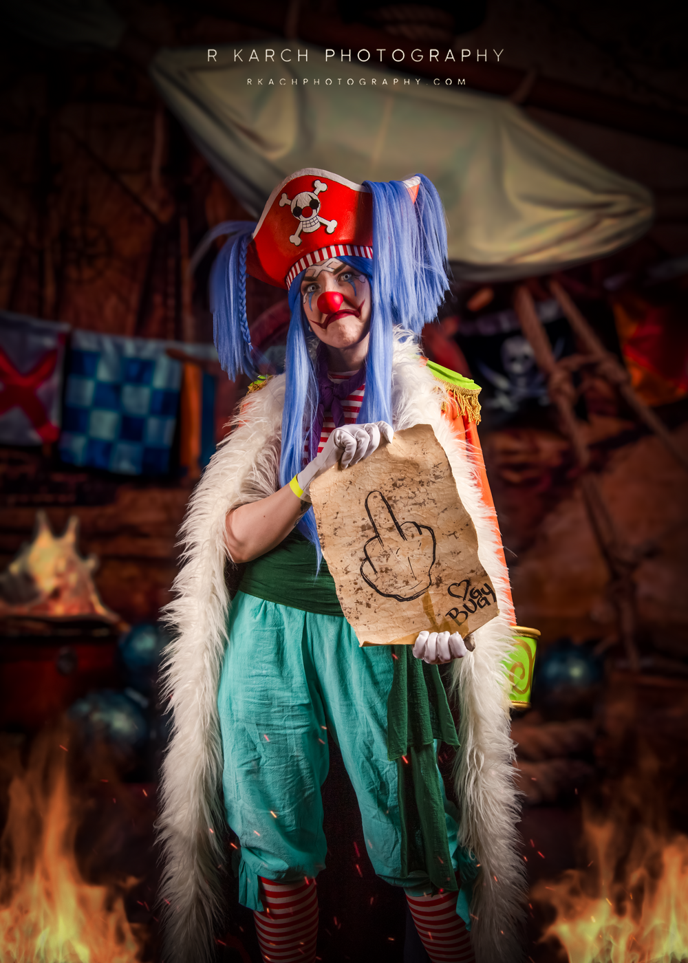 Whimsical cosplay character in blue wig and pirate hat holds up a scroll in medieval fantasy setting.