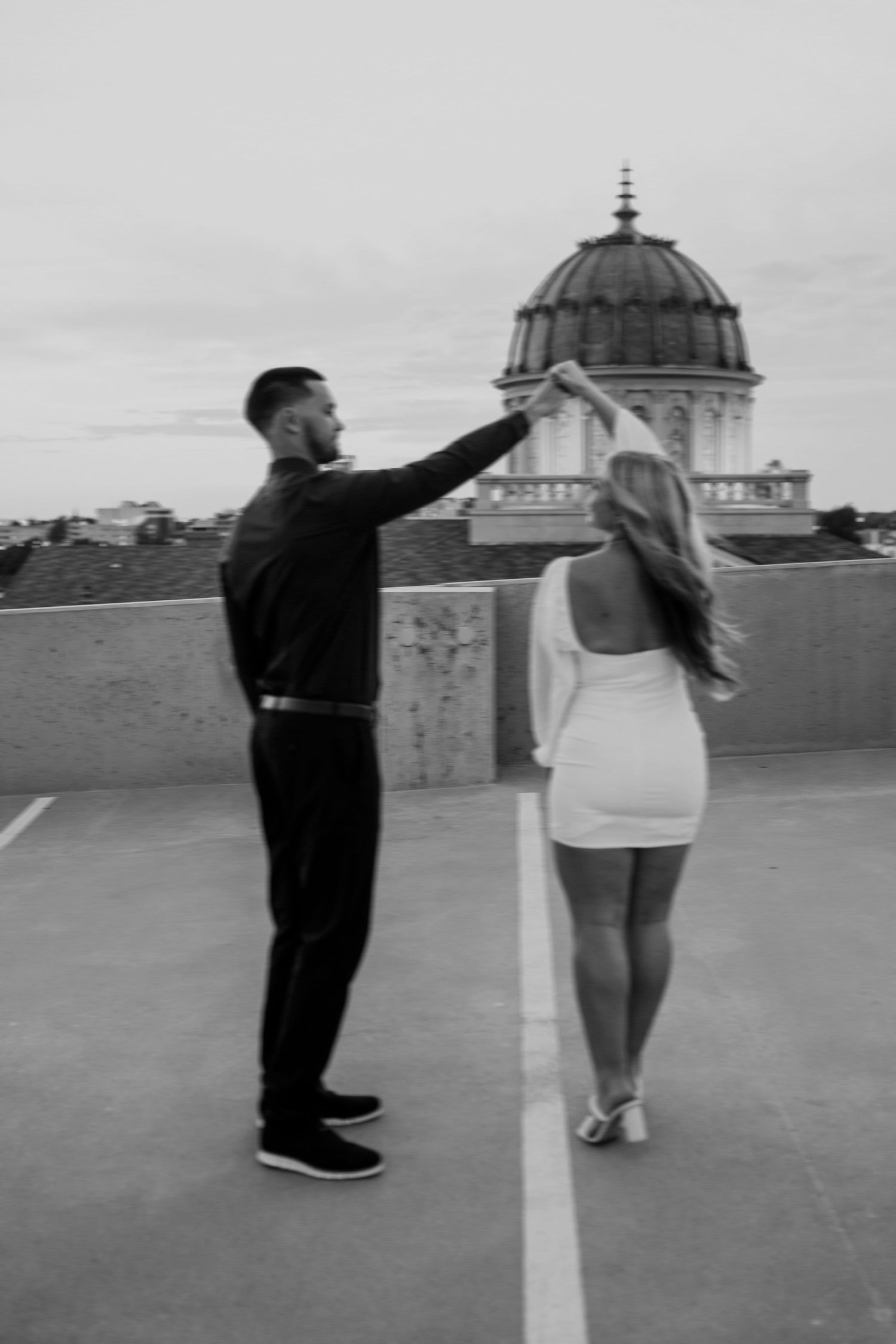 A black and white photo of a couple posing by a domed building architecture.