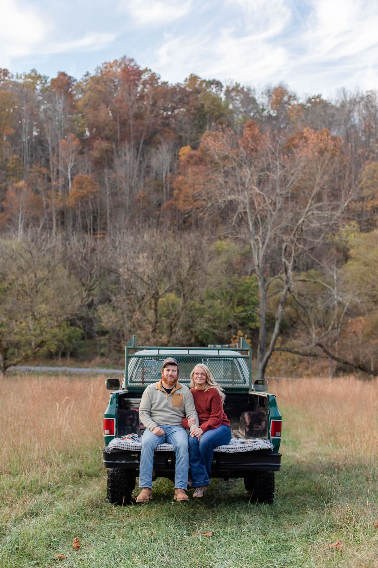 Couple relaxing in the bed of a turquoise pickup truck in a rustic autumn field.