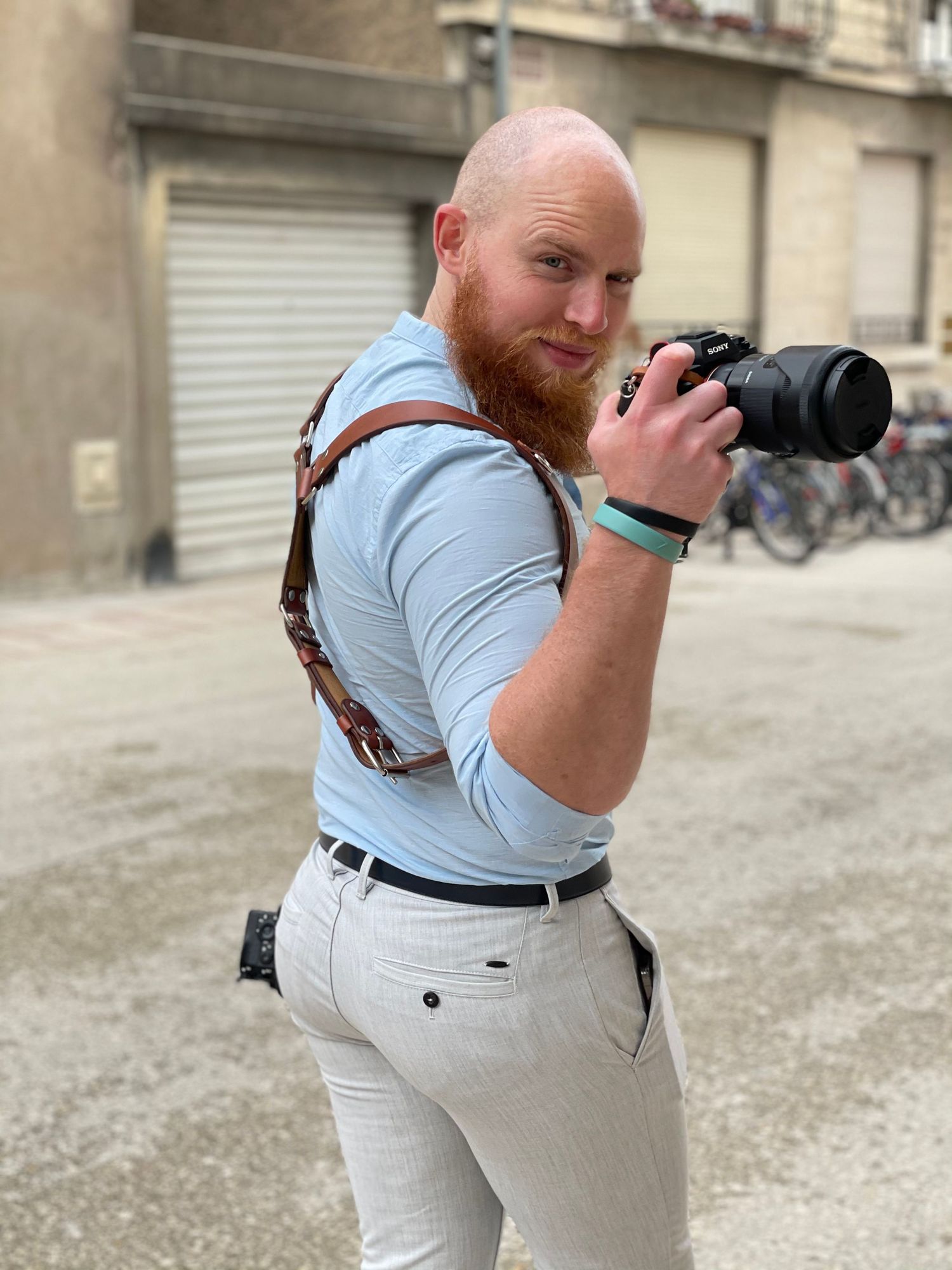 Professional photographer with red beard and camera gear on urban street.