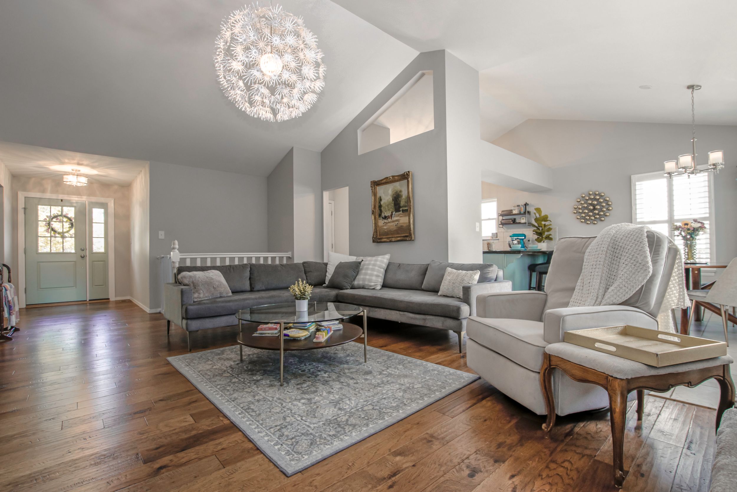 Contemporary living space with grey sectionals, crystal chandelier, and hardwood flooring.