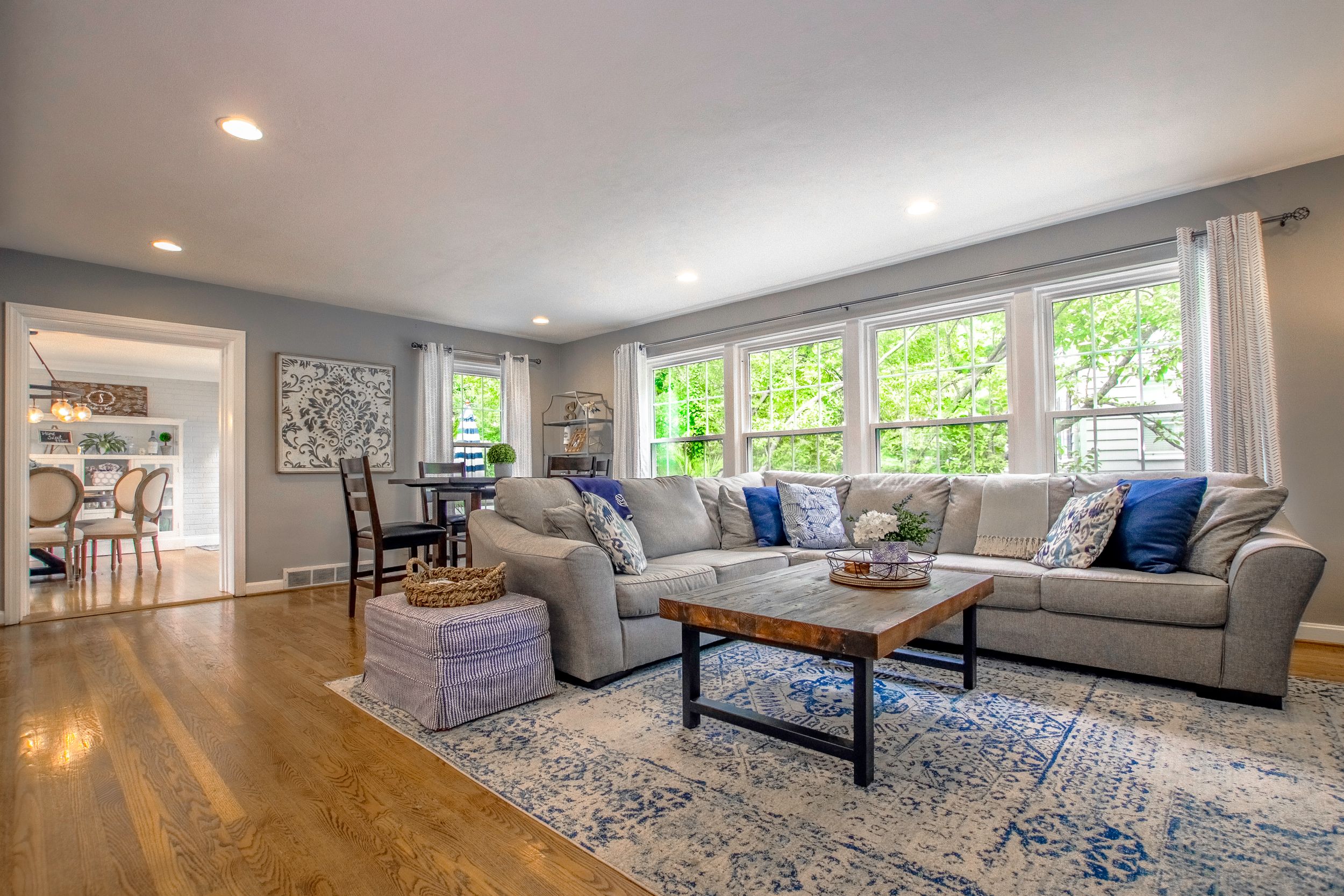 Modern living room with beige sectional sofa, blue accents, and hardwood floors in an open concept space.