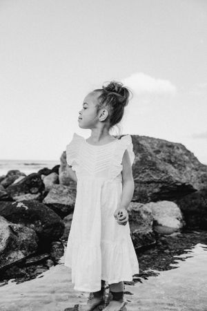 A small child in a white dress explores rocky coastal terrain.