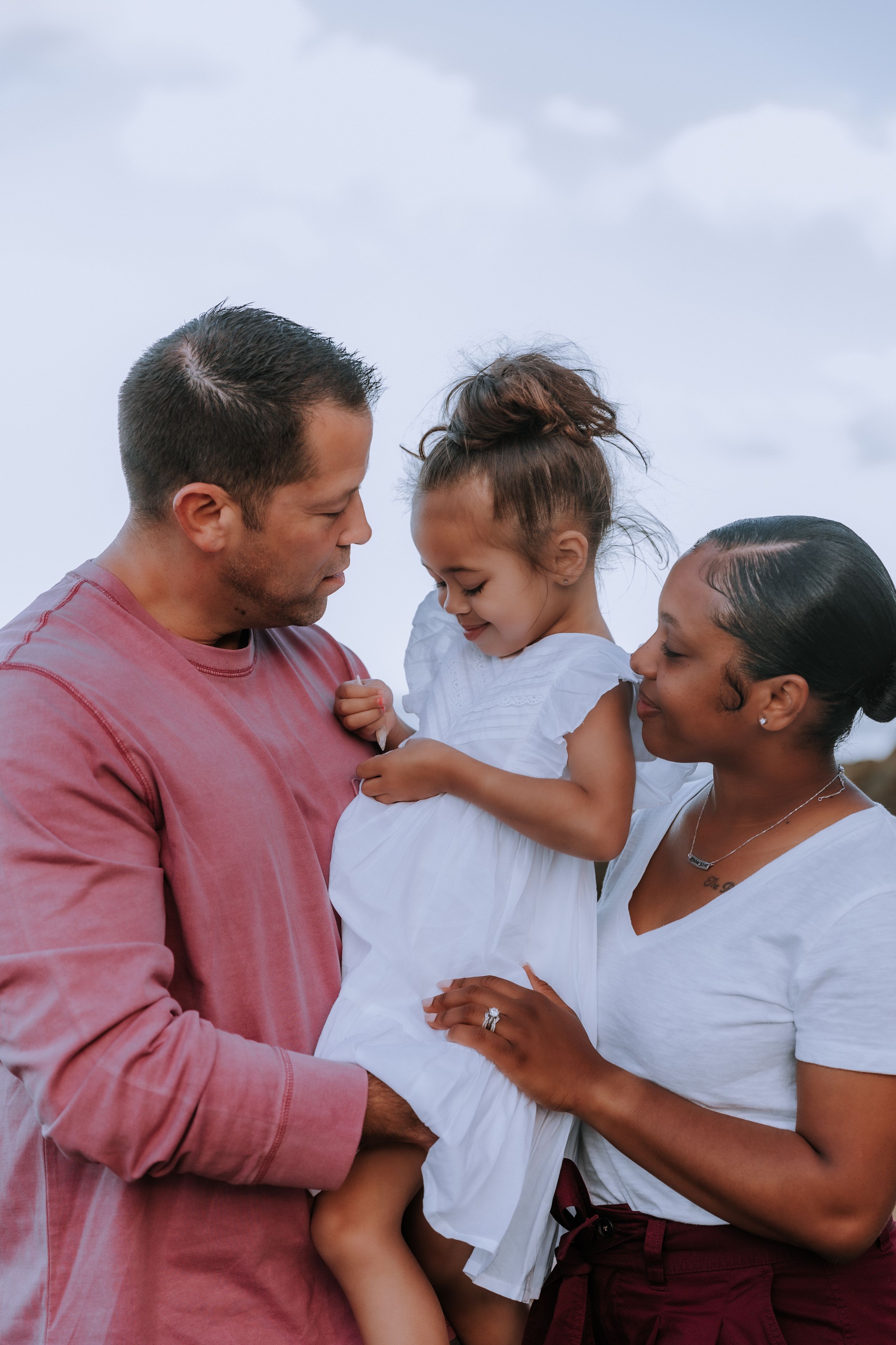 A joyful family plays and laughs together against a cloudy sky background.