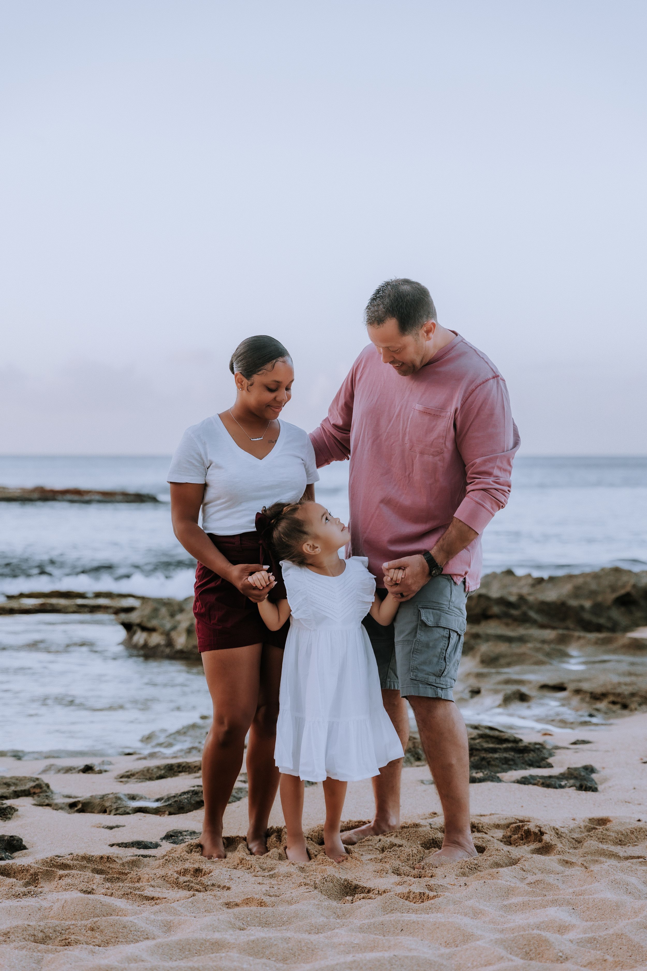 A family shares a tender moment together on a rocky beach at sunset.