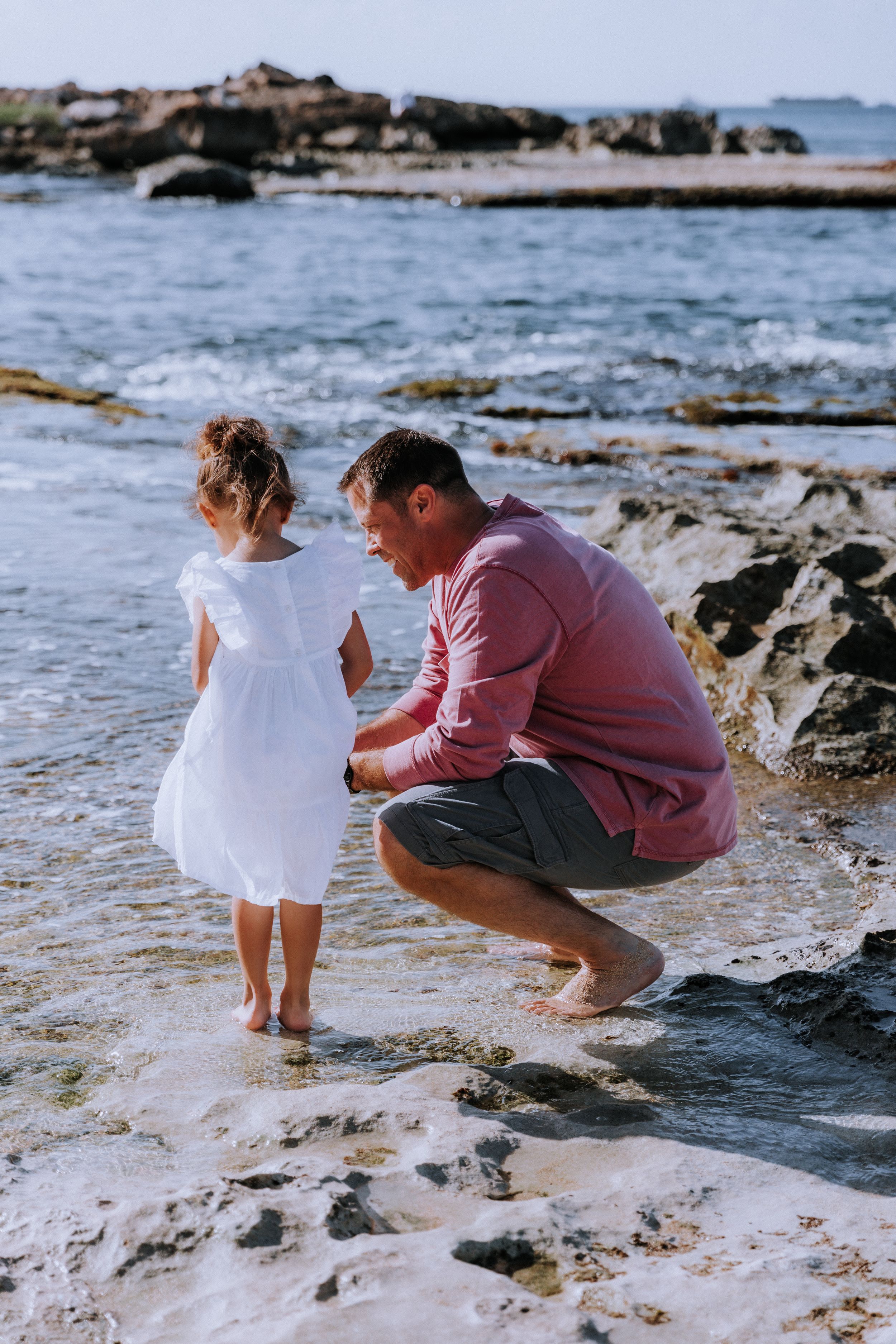 Parent and child exploring tide pools together on rocky beach.