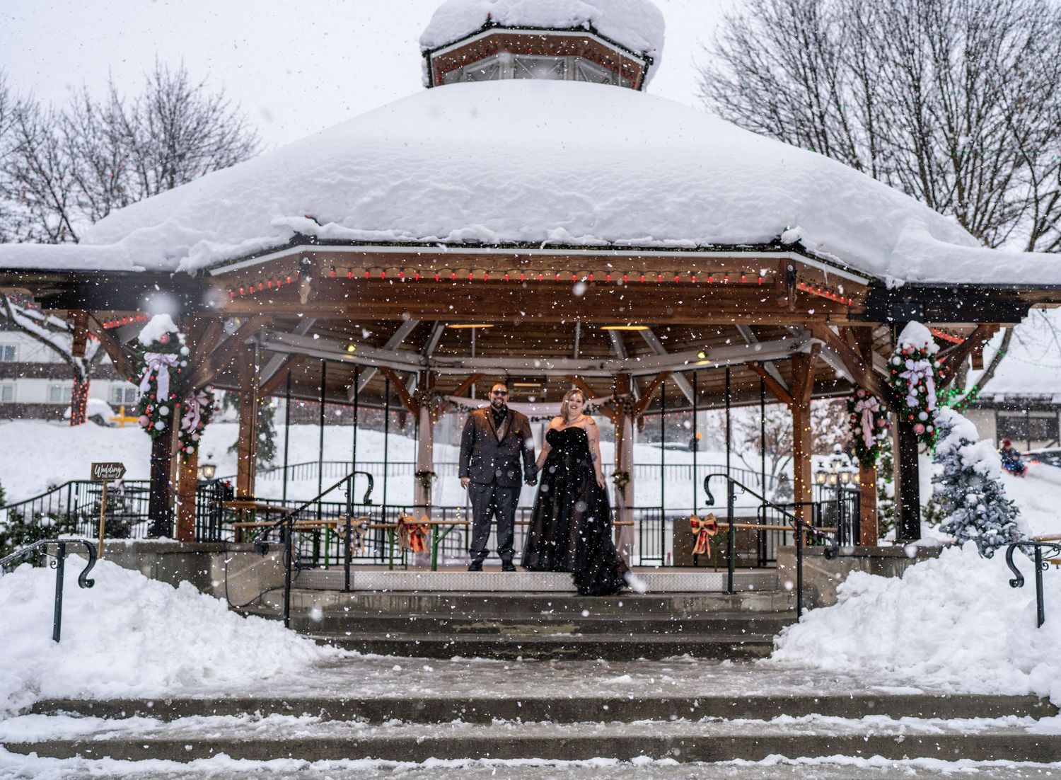 Snow-covered wooden gazebo decorated for winter with festive decorations in a peaceful park setting.