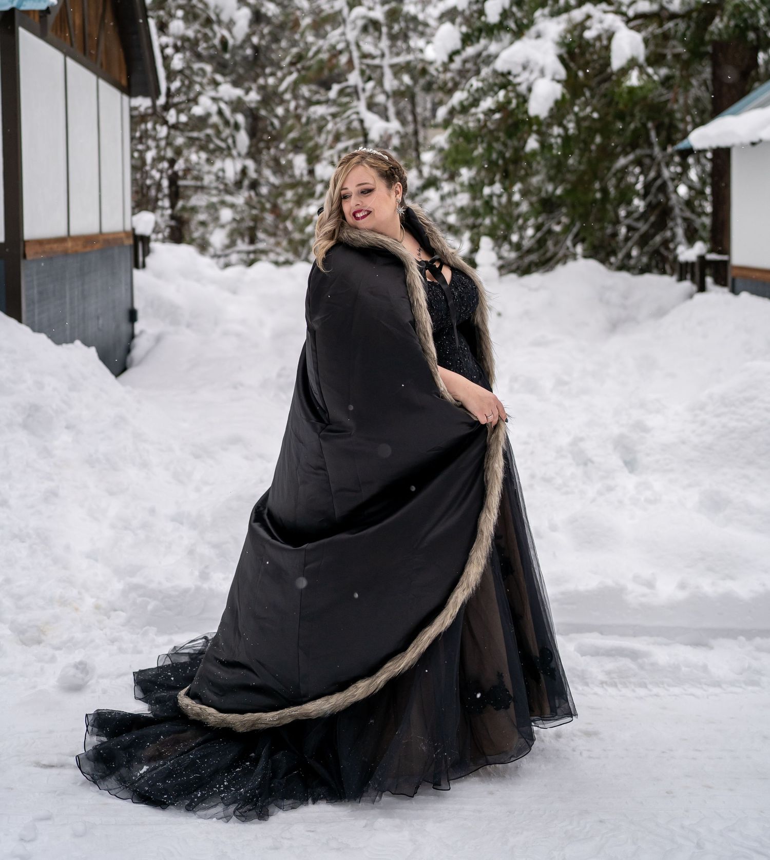 Person in flowing black formal dress poses dramatically in snowy winter setting.