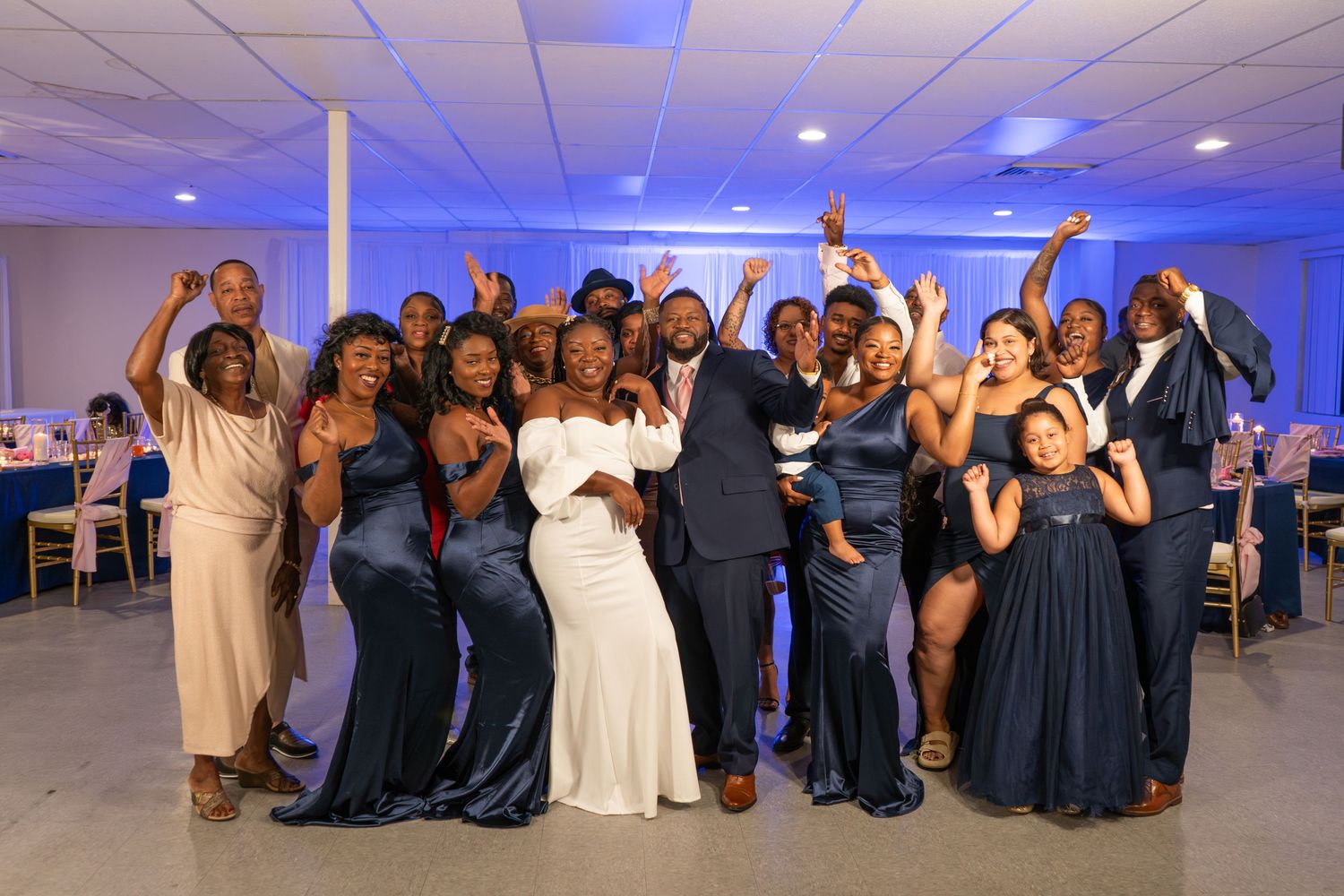 Large celebratory group photo at a formal wedding reception with navy and white attire.
