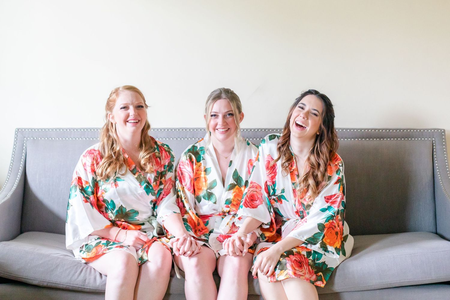 Three people in floral print robes laughing together on a gray sofa.