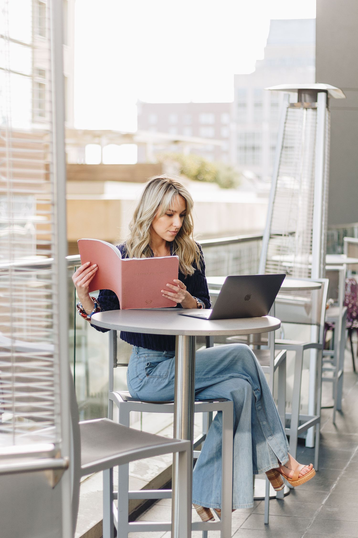 Person working outdoors at high table with laptop and folder on urban patio.
