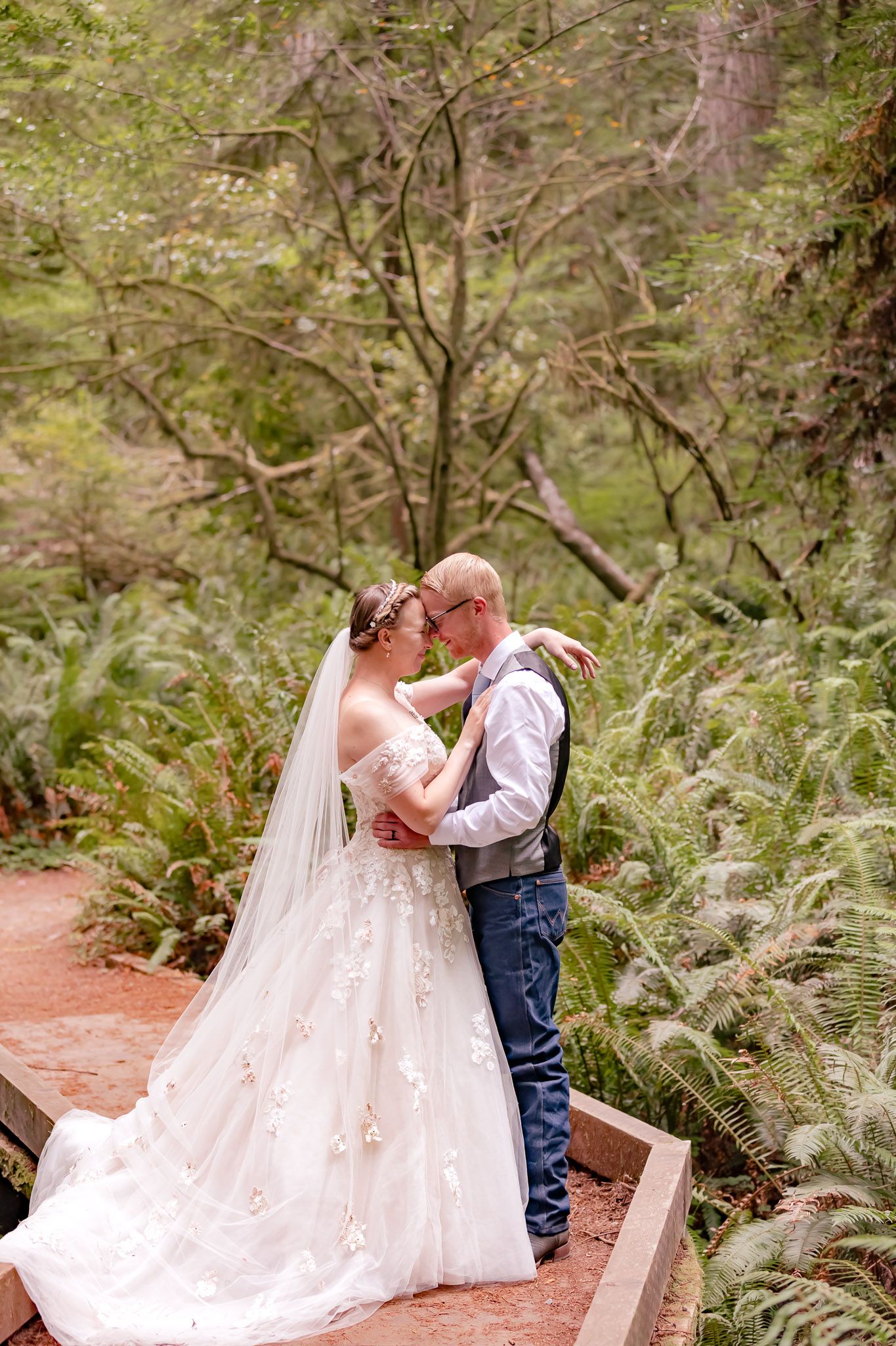 Bride and Groom share an intimate moment with foreheads touching. Photographer captures them in a fern forest at the California Redwoods