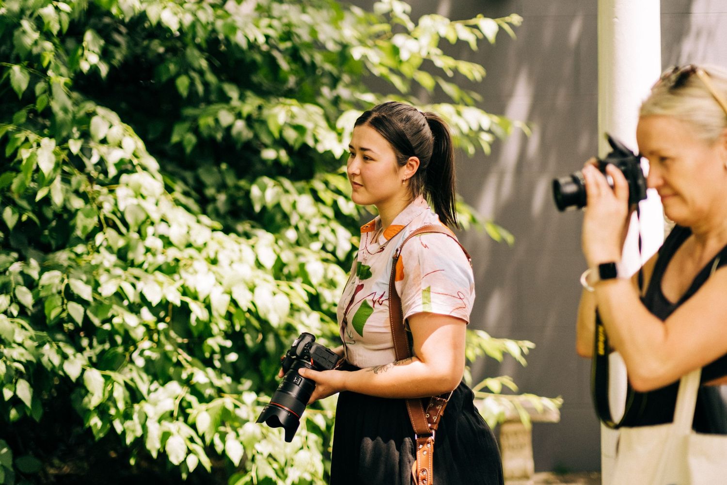 Two photographers shooting photos outdoors in a garden setting with natural lighting.