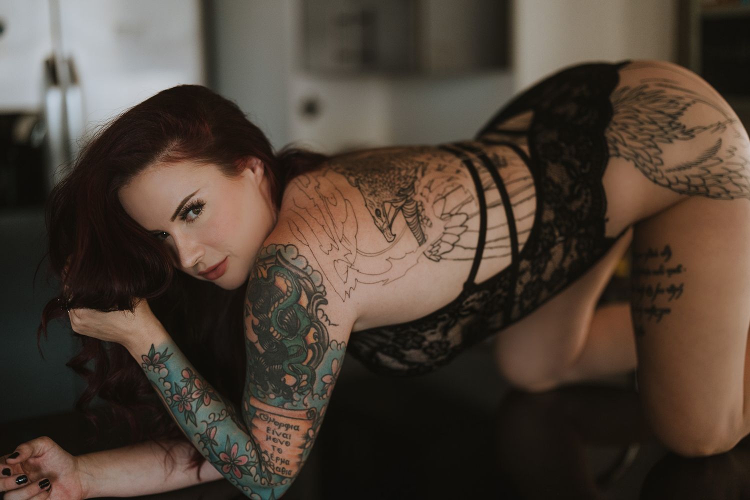 An artistic boudoir photograph showcasing intricate tattoo work and black lace lingerie.