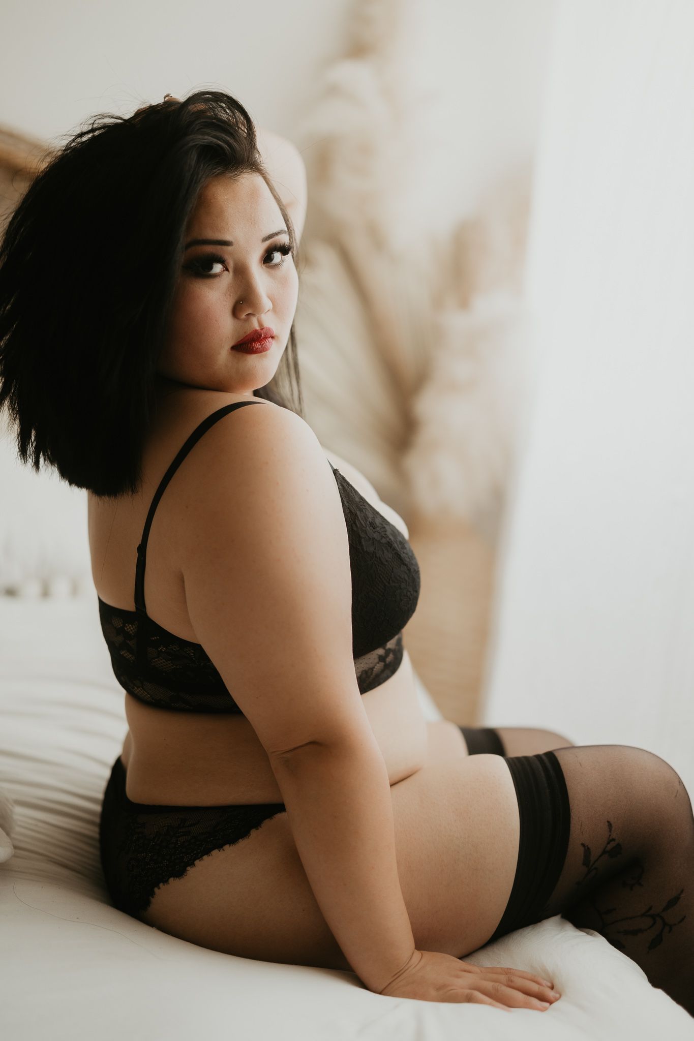 Boudoir photo of woman in black lingerie posing on white bedding.