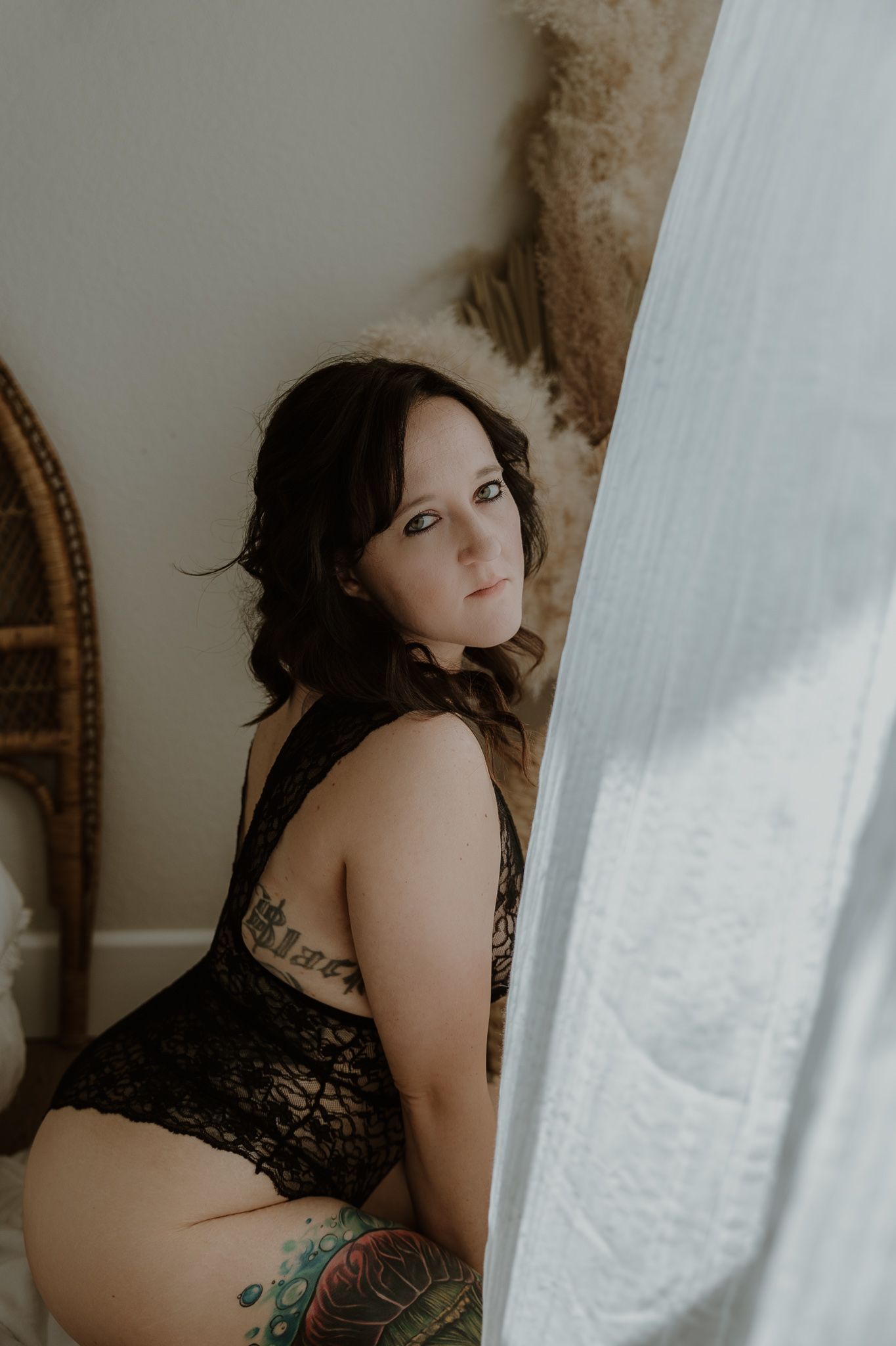 Boudoir photography featuring woman in black lingerie by window with natural light.