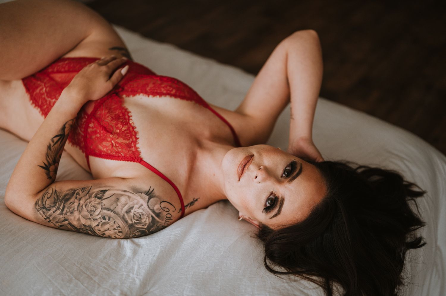 Moody boudoir photo of person in red lace lingerie with tattoos.