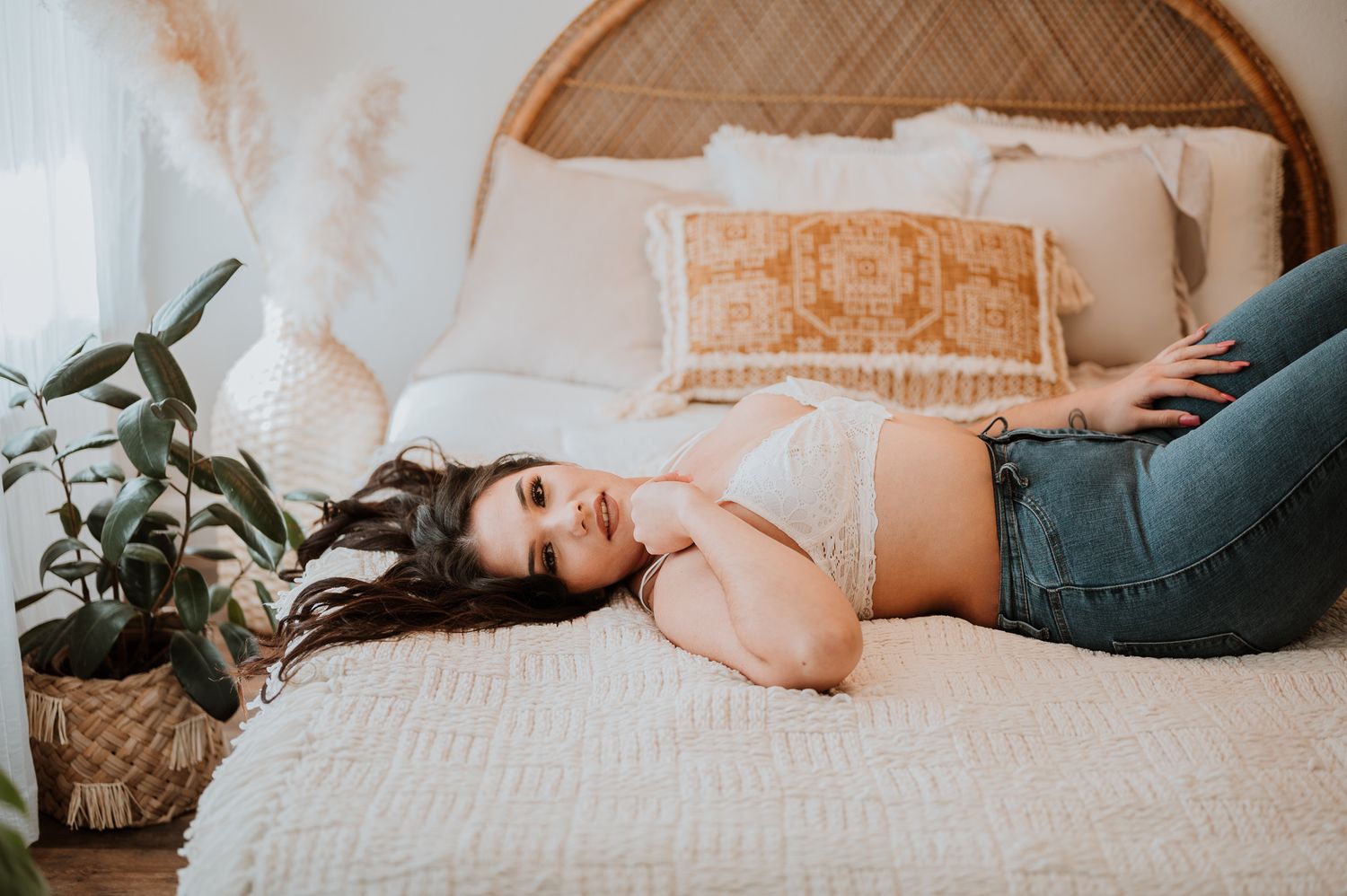 Person lying on bed wearing casual denim and crop top near potted plant.