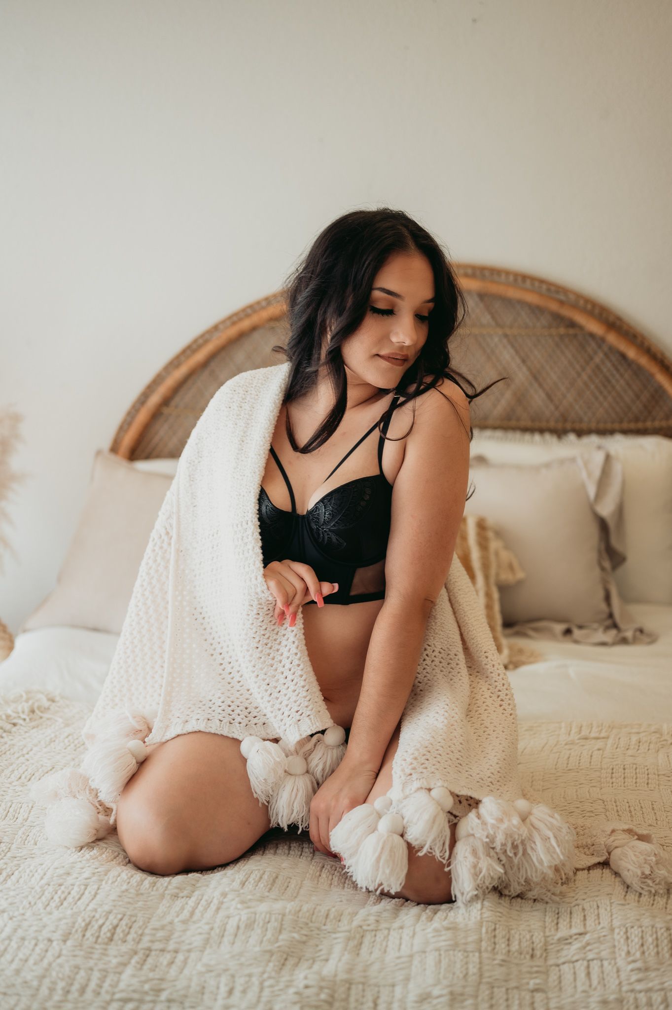 Person in black lingerie and white cardigan kneeling on textured bedding.