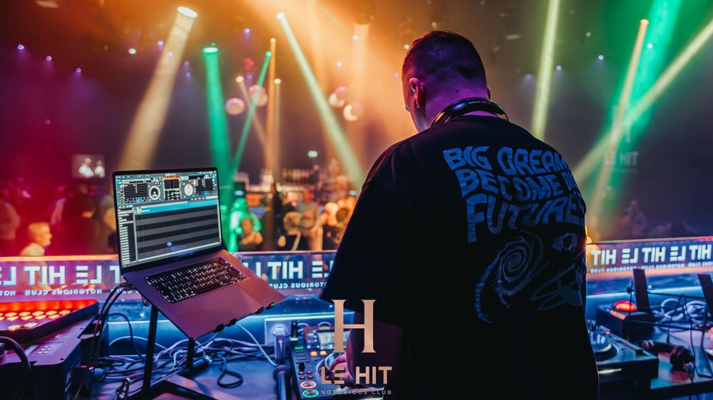 DJ performing at a vibrant nightclub with colorful stage lights and a crowd in the background.