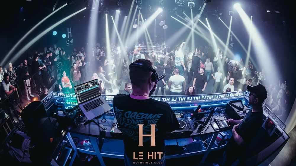 DJ at Le Hit club mixing music for a packed dance floor under dramatic blue lighting.