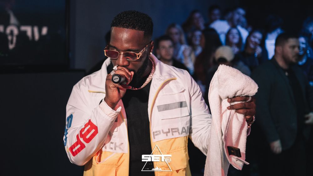 Male artist in white Pyramid jacket performing at a nightclub event.