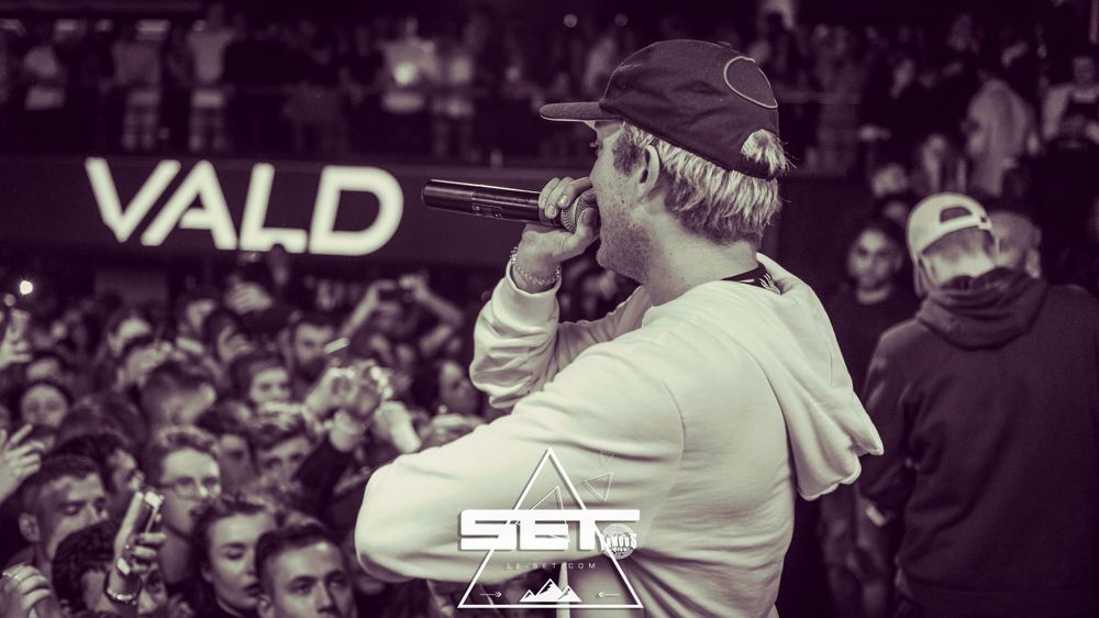 Black and white photo of rapper Vald performing live on stage with microphone for crowd.