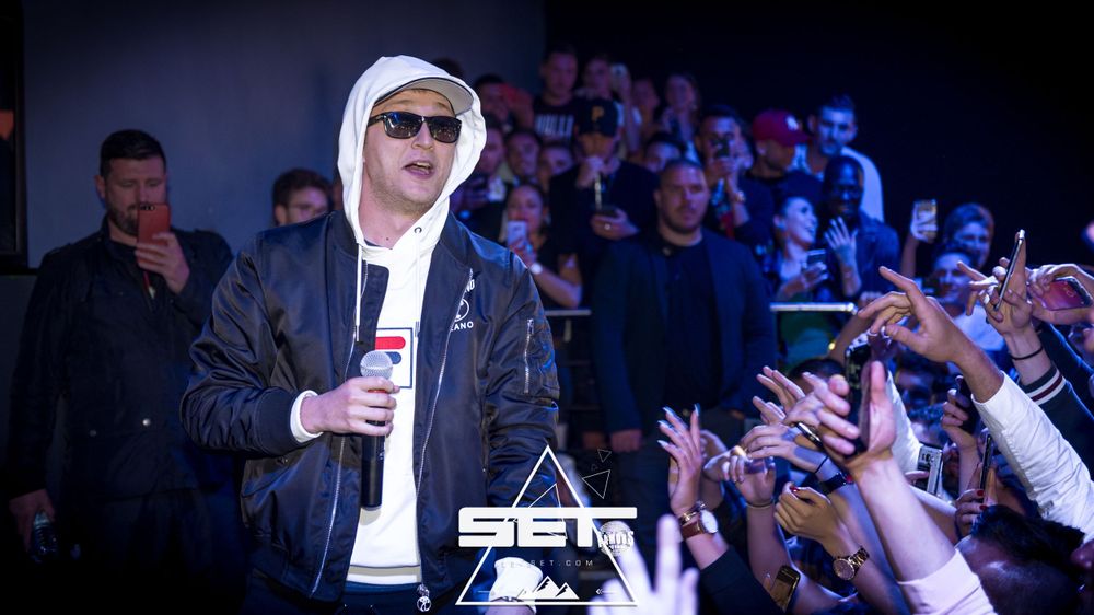 Male rapper in white hoodie and sunglasses performing on stage reaching out to fans.