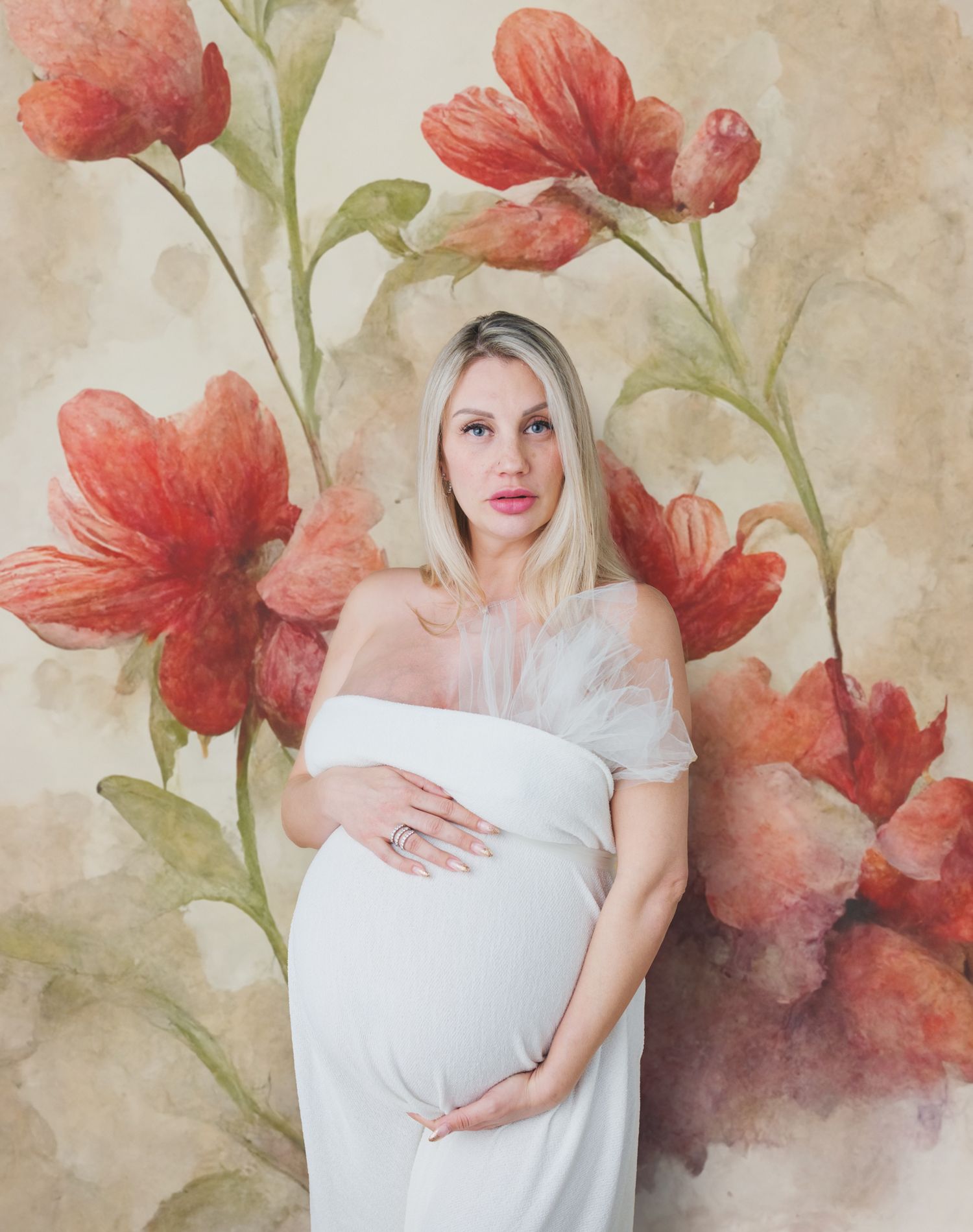Artistic maternity photo with a white dress against a watercolor floral backdrop of large red poppies.