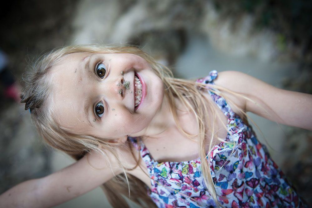 A joyful child in a floral dress with blonde hair smiling at the camera.