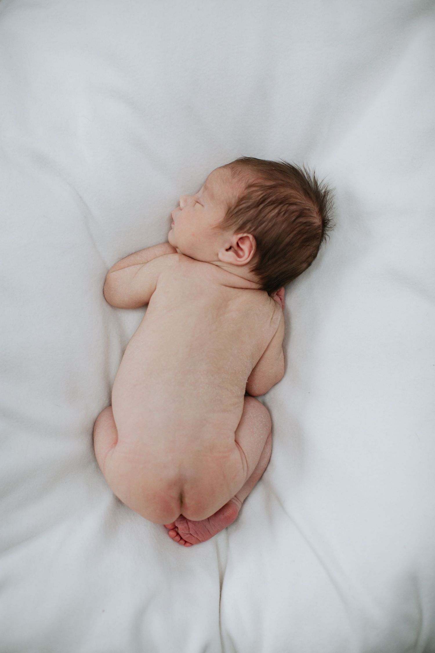 Newborn baby sleeping peacefully on soft white bedding viewed from above.