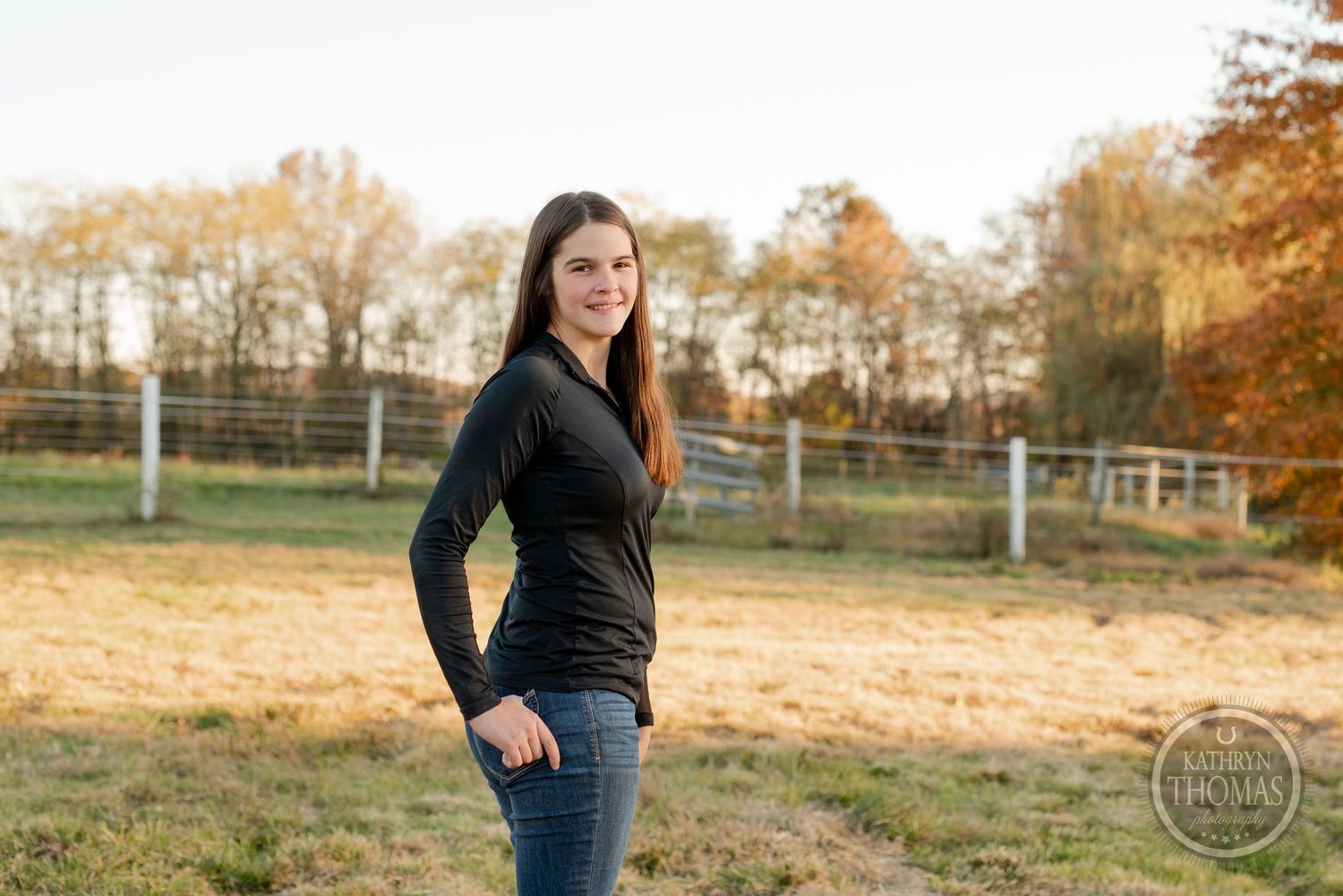 Casual autumn portrait with hands in pockets against golden field and trees.