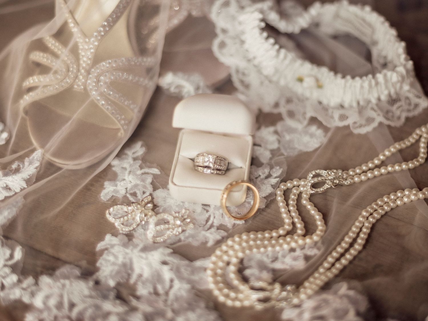 Vintage-style wedding accessories including pearls, lace and jewelry arranged on neutral background.