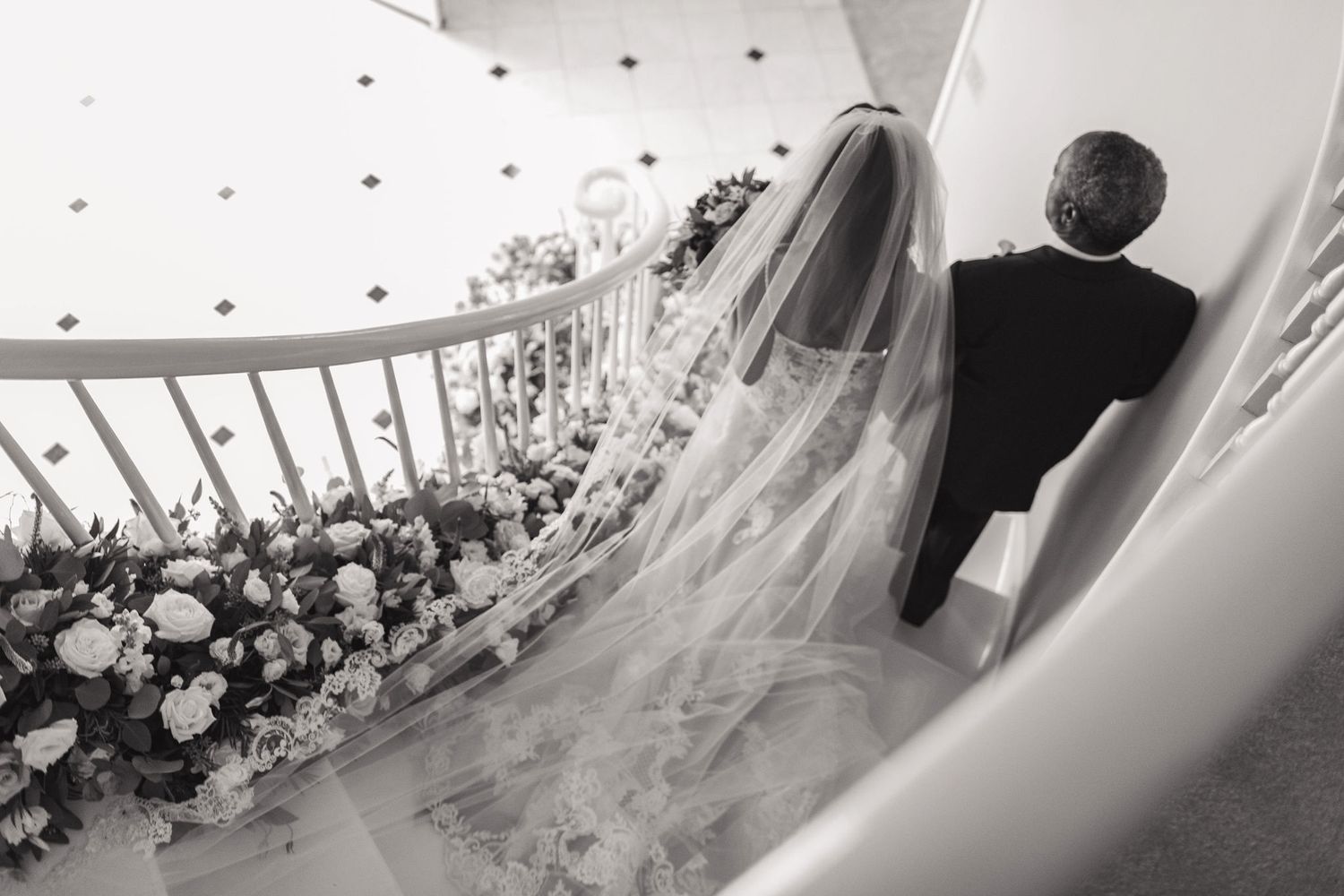 A black and white photo of a wedding dress train with floral decorations along a curved railing.