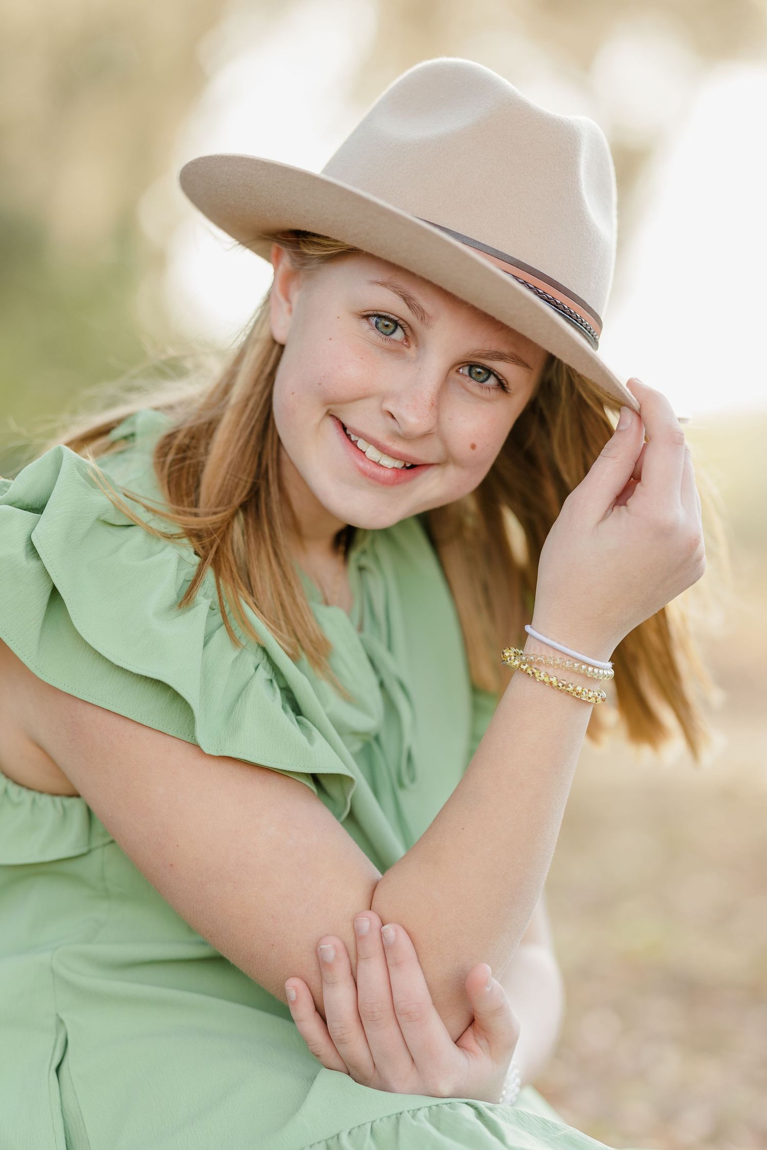 Portrait of person in green blouse and tan hat smiling outdoors.