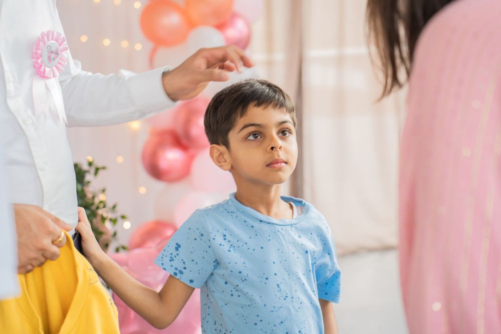Child in blue t-shirt stands at a party with pink balloon decorations.