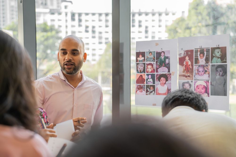 People gather in a meeting room with photos displayed on the wall during a discussion.