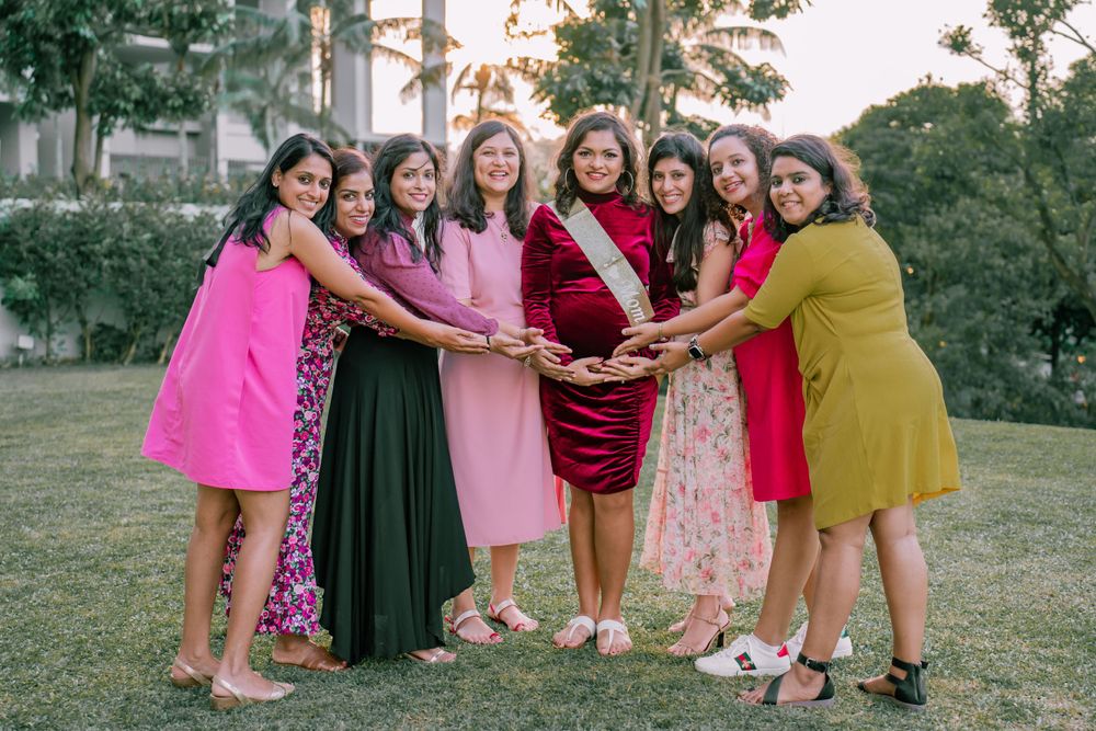 A group of friends wearing colorful dresses stand together in a garden, joining hands in a circle formation.