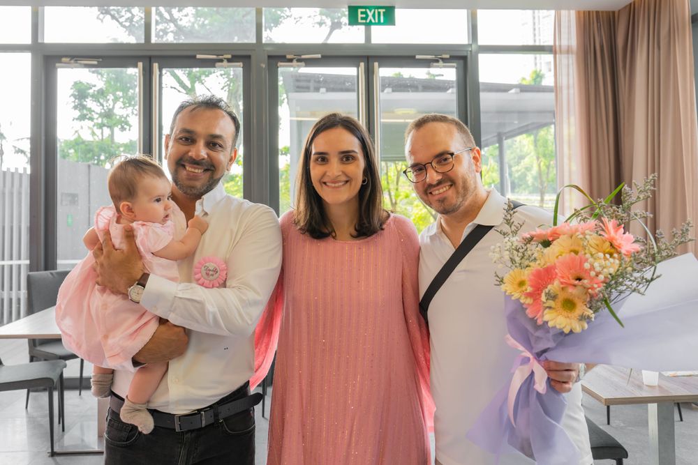 A group gathers indoors for a celebration with a baby and flowers.