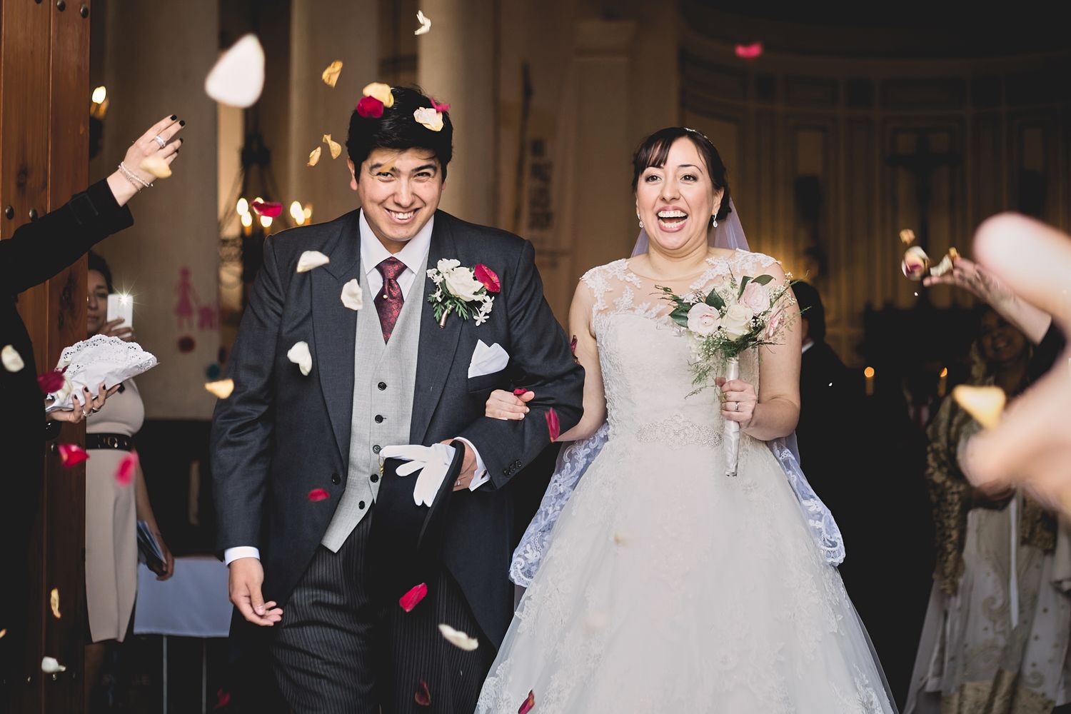 Joyful newlyweds exit their ceremony while guests shower them with flower petals.