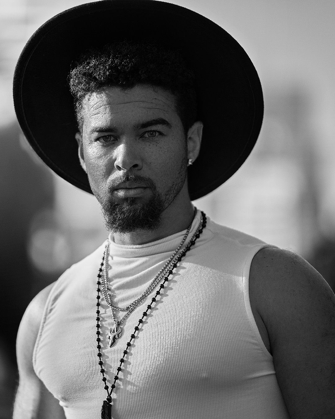 Black and white portrait featuring someone in a wide-brimmed hat and beaded necklace wearing a white tank top.
