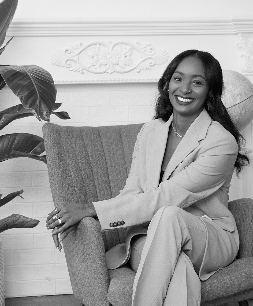 Elegant portrait in cream suit seated on grey couch with decorative wall molding.