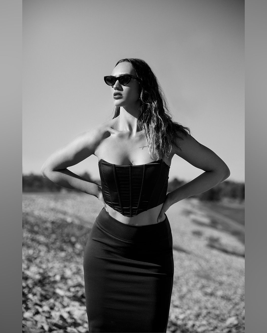 Black and white fashion photo of a person in a fitted crop top and skirt outdoors.