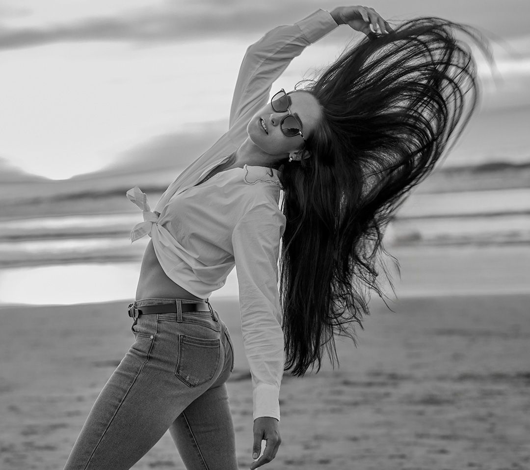 Black and white image of a person with flowing hair flipping their head back on a beach.