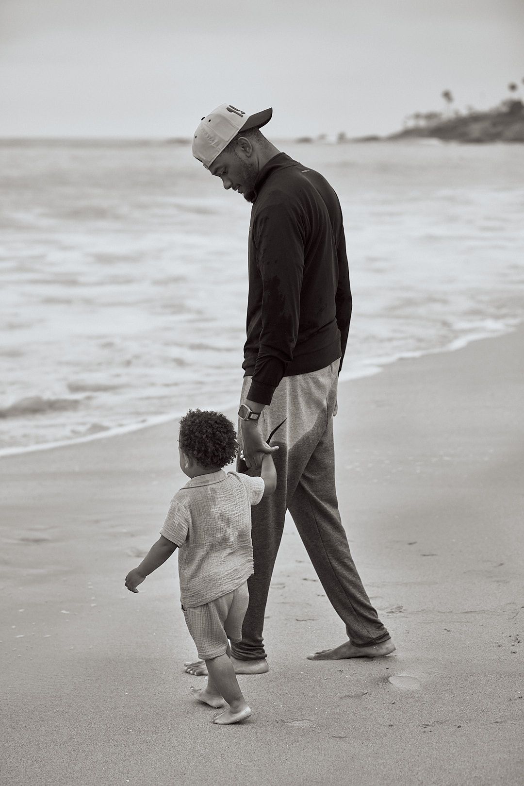 Tender moment captured of adult and child walking hand in hand along beach at sunset.