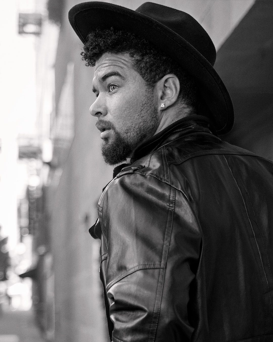 Black and white profile shot of person in leather jacket and wide-brim hat.