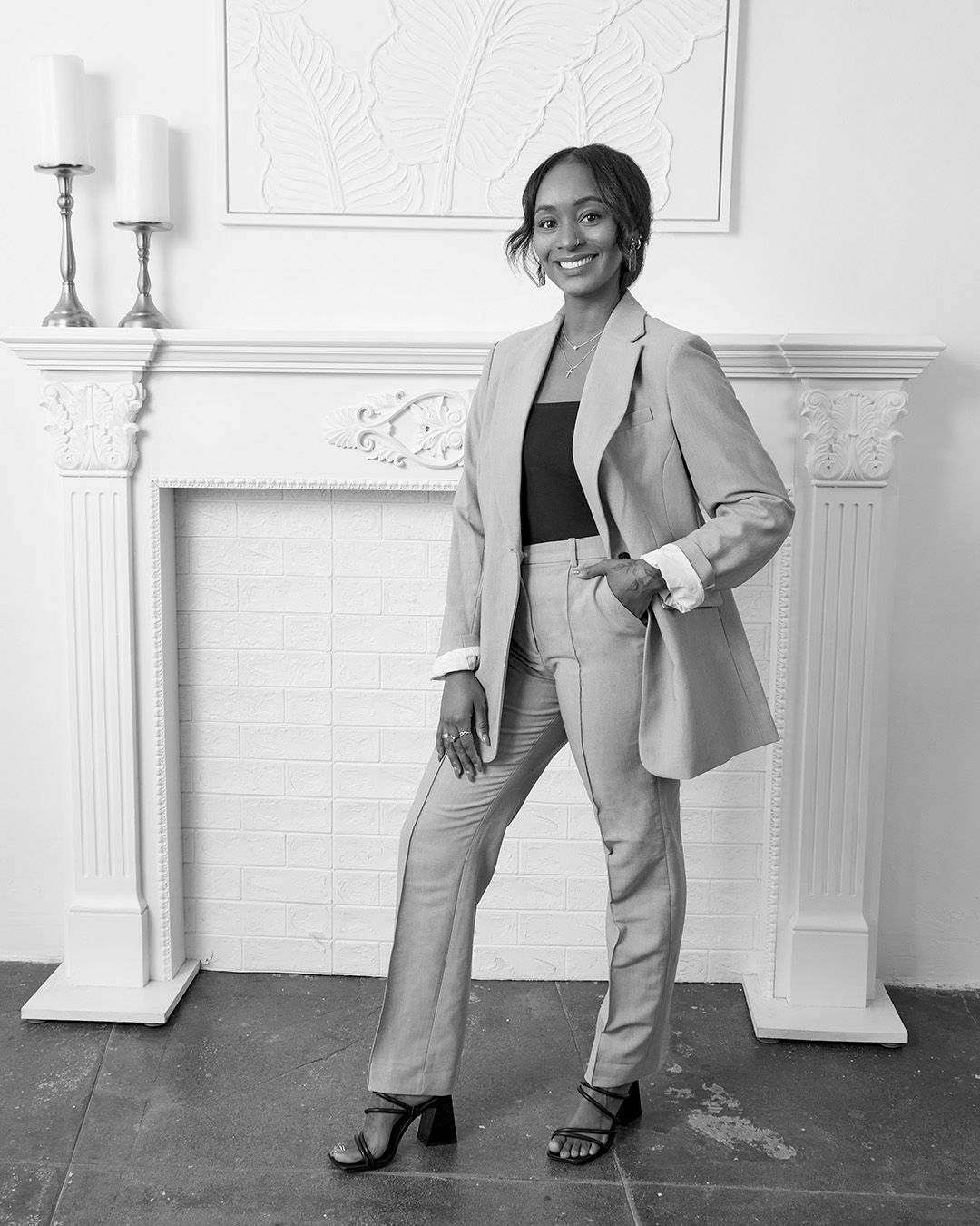 Professional portrait in a light suit standing by an elegant white fireplace.